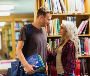 Side view of a smiling young couple against bookshelf in the library