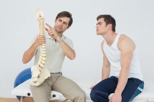 Male physiotherapist showing patient something on skeleton model in medical office