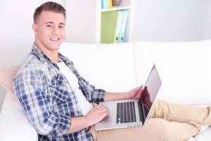 Handsome young man sitting on couch with laptop in room