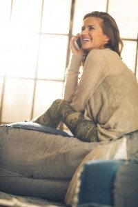 Happy young woman talking cell phone in loft apartment