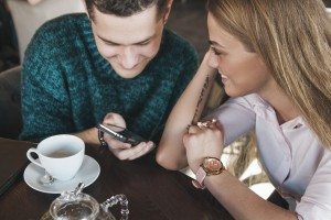 Young couple surfing the web looking at photos on mobile phone. In a cafe.