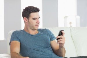 Handsome man relaxing on couch texting in bright living room